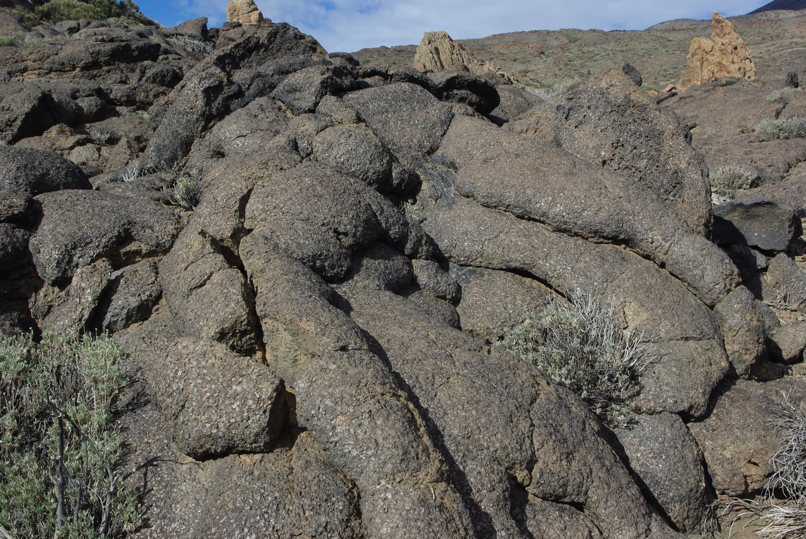 Coladas de lava pahoehoe solidificadas en Las Cañadas del Teide, con la roca oscura formando pliegues y roques claros al fondo, Parque Nacional del Teide, Tenerife