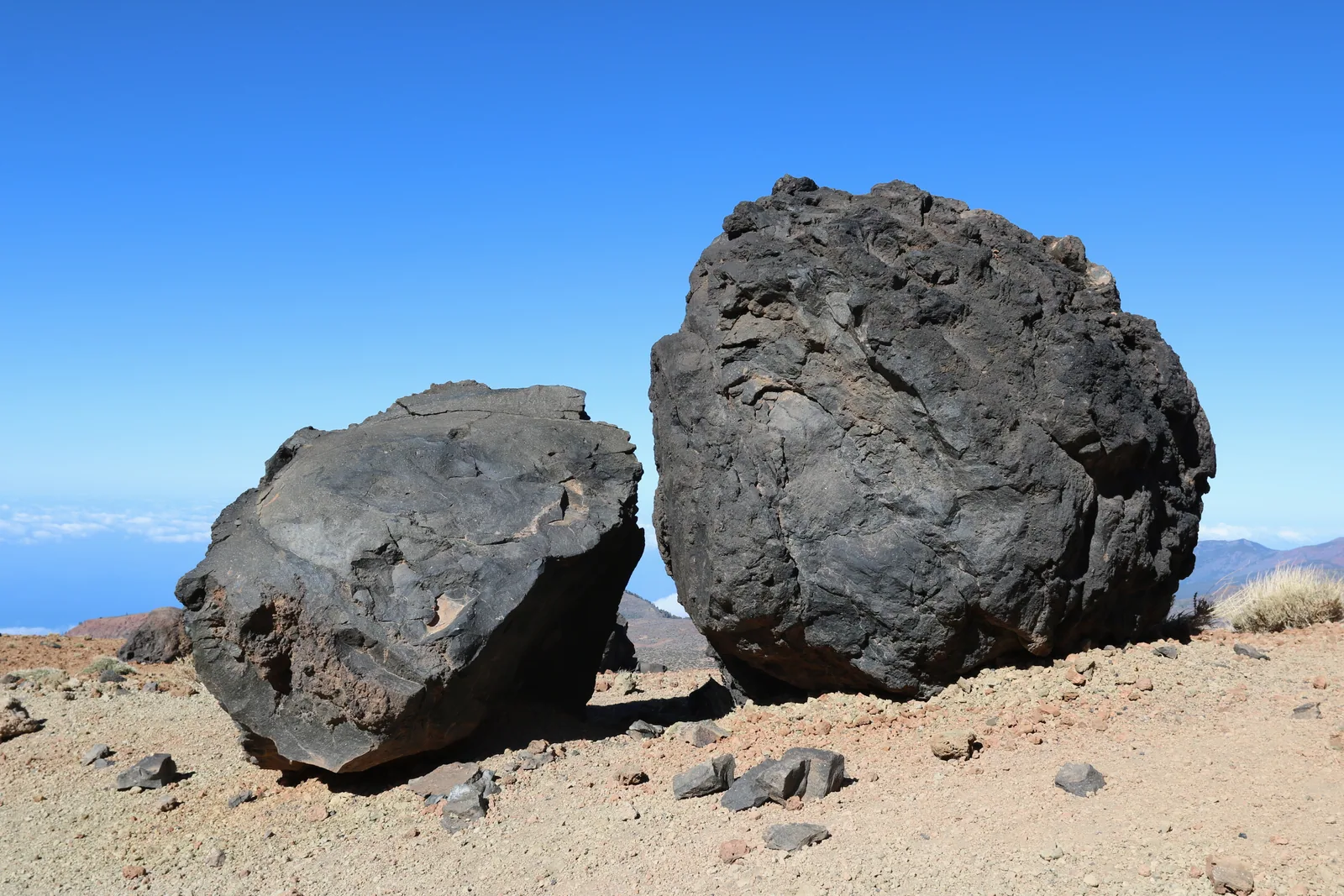 Dos «huevos del Teide», bolas oscuras de lava acrecionada, posadas sobre el terreno claro de pómez y lapilli en la ladera de Montaña Blanca, con el mar de nubes al fondo (Parque Nacional del Teide, Tenerife)